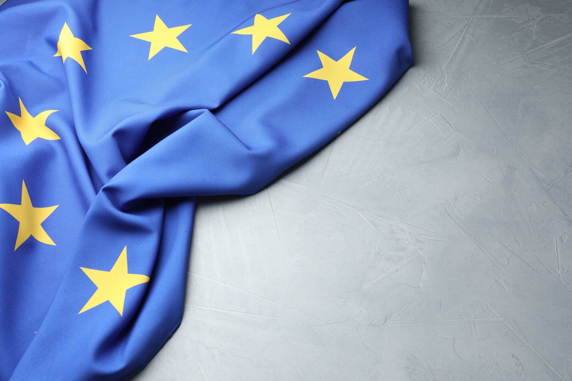 Blue flag with yellow stars, representing the European Union, is partially spread out on a gray surface.